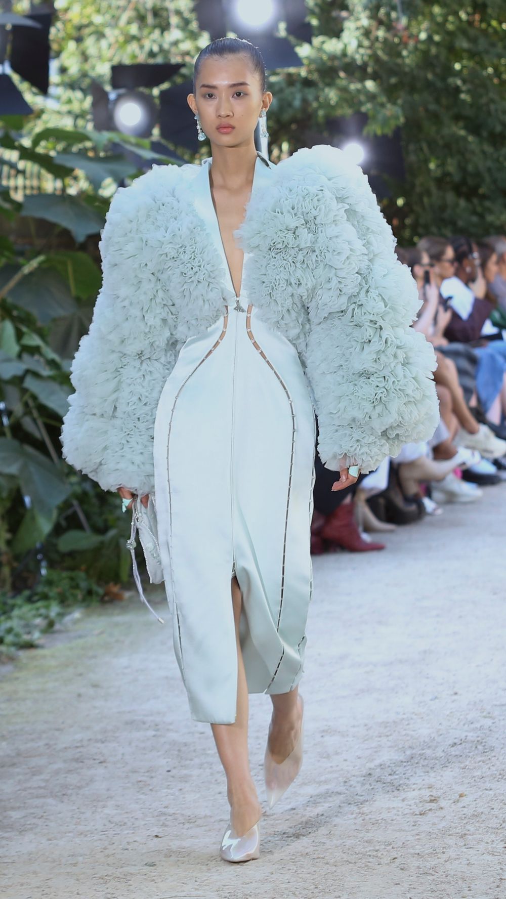 Fashion model walking runway in avant-garde white dress with dramatic puffy sleeves.
