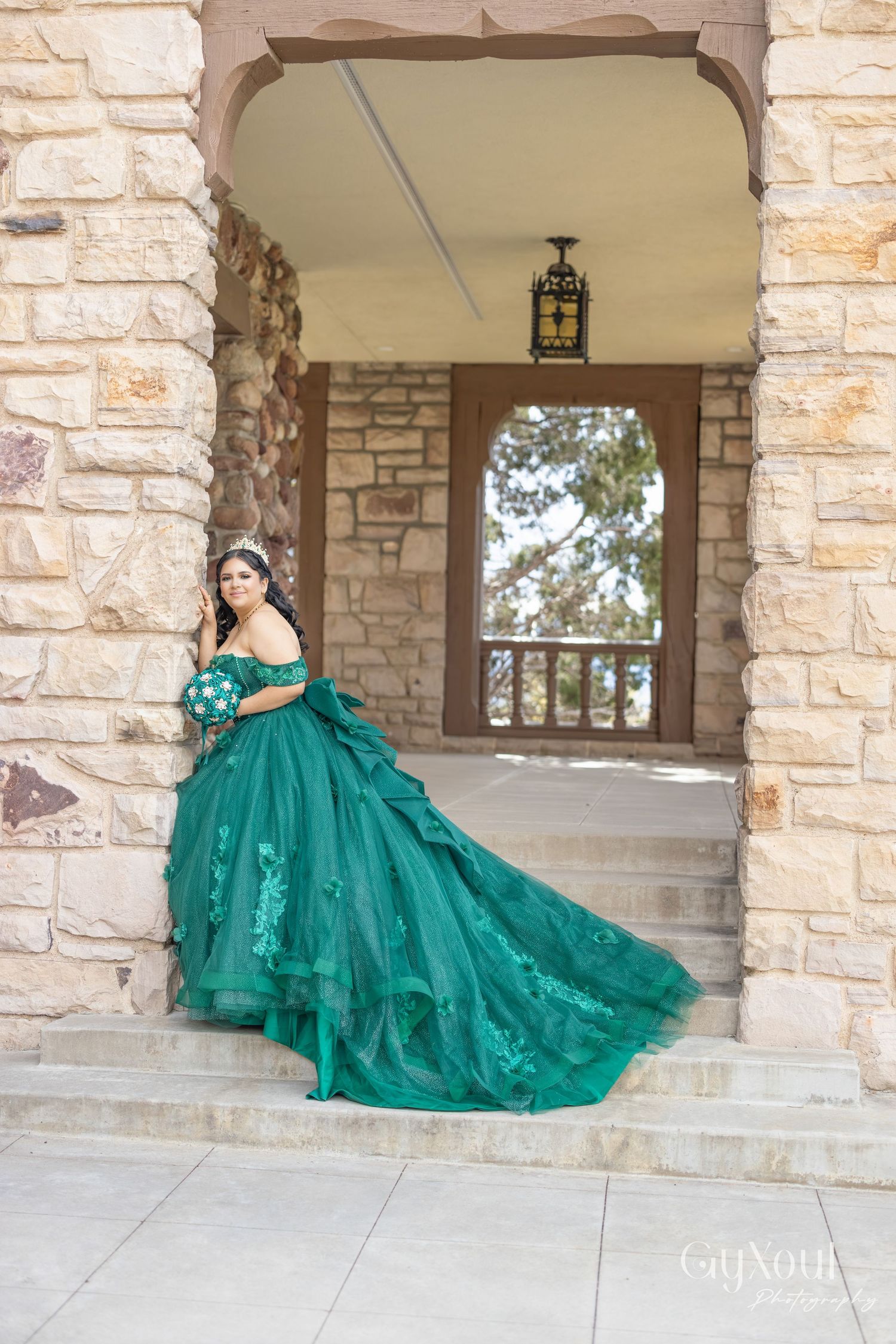 A flowing emerald green ball gown is beautifully displayed across stone arches in an outdoor setting.