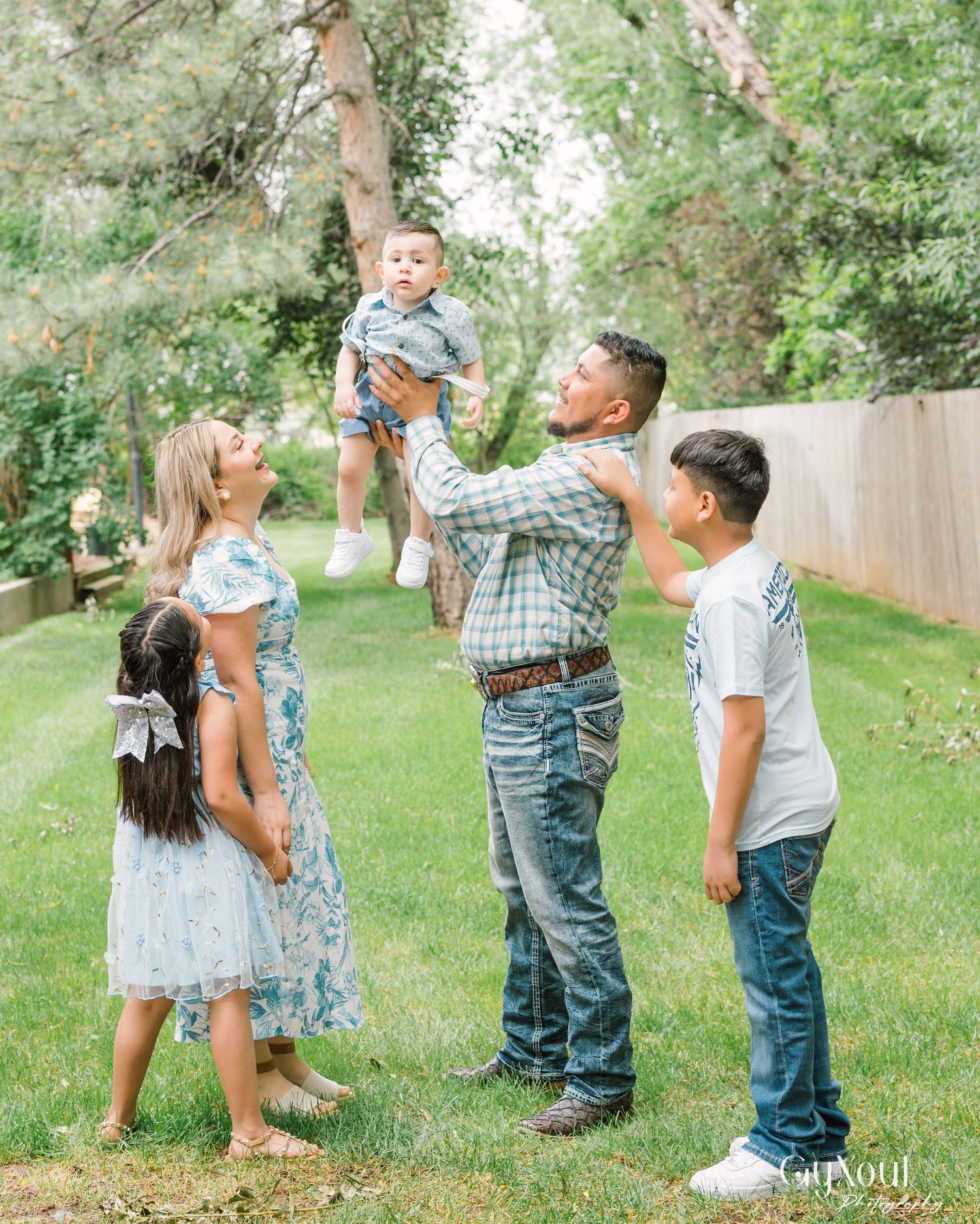 A family plays together in a grassy backyard while taking cheerful candid photos during a sunny summer day.