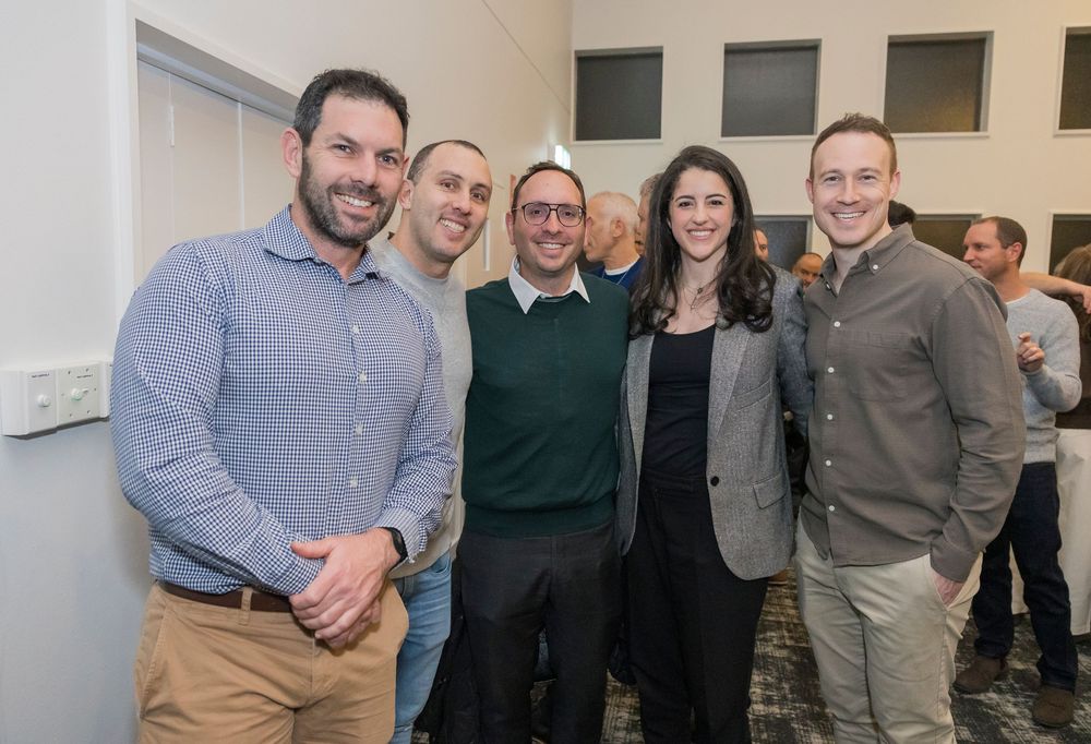 A group of business professionals smile while posing together at an indoor office gathering.
