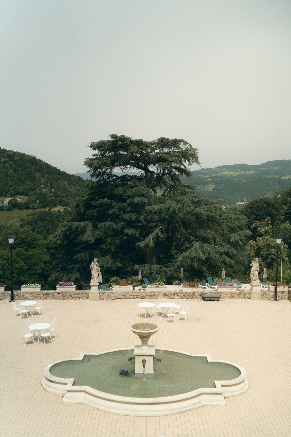 Large formal garden plaza with fountains and statues surrounded by trees.