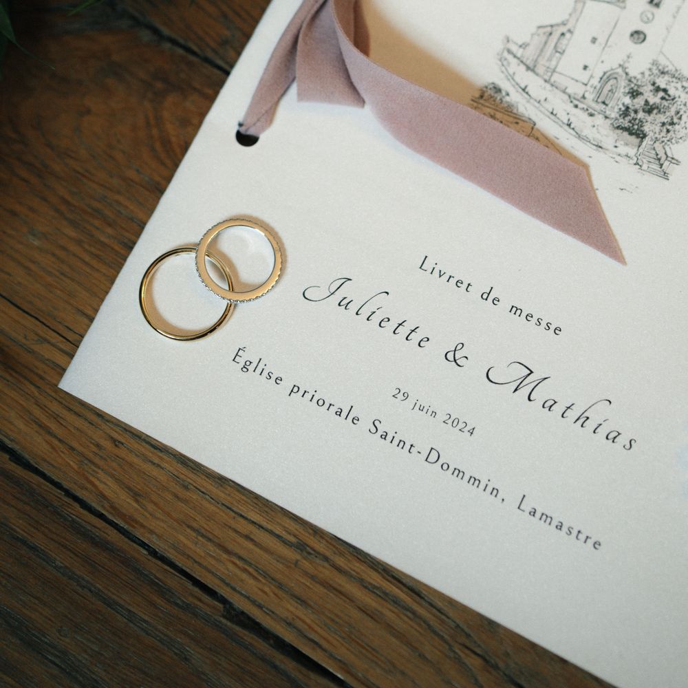 Wedding invitation with gold rings and elegant calligraphy on wooden surface.