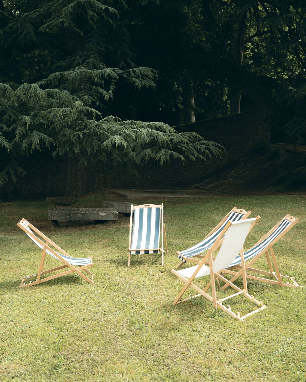 Several striped beach chairs arranged on a grassy lawn in a garden setting.