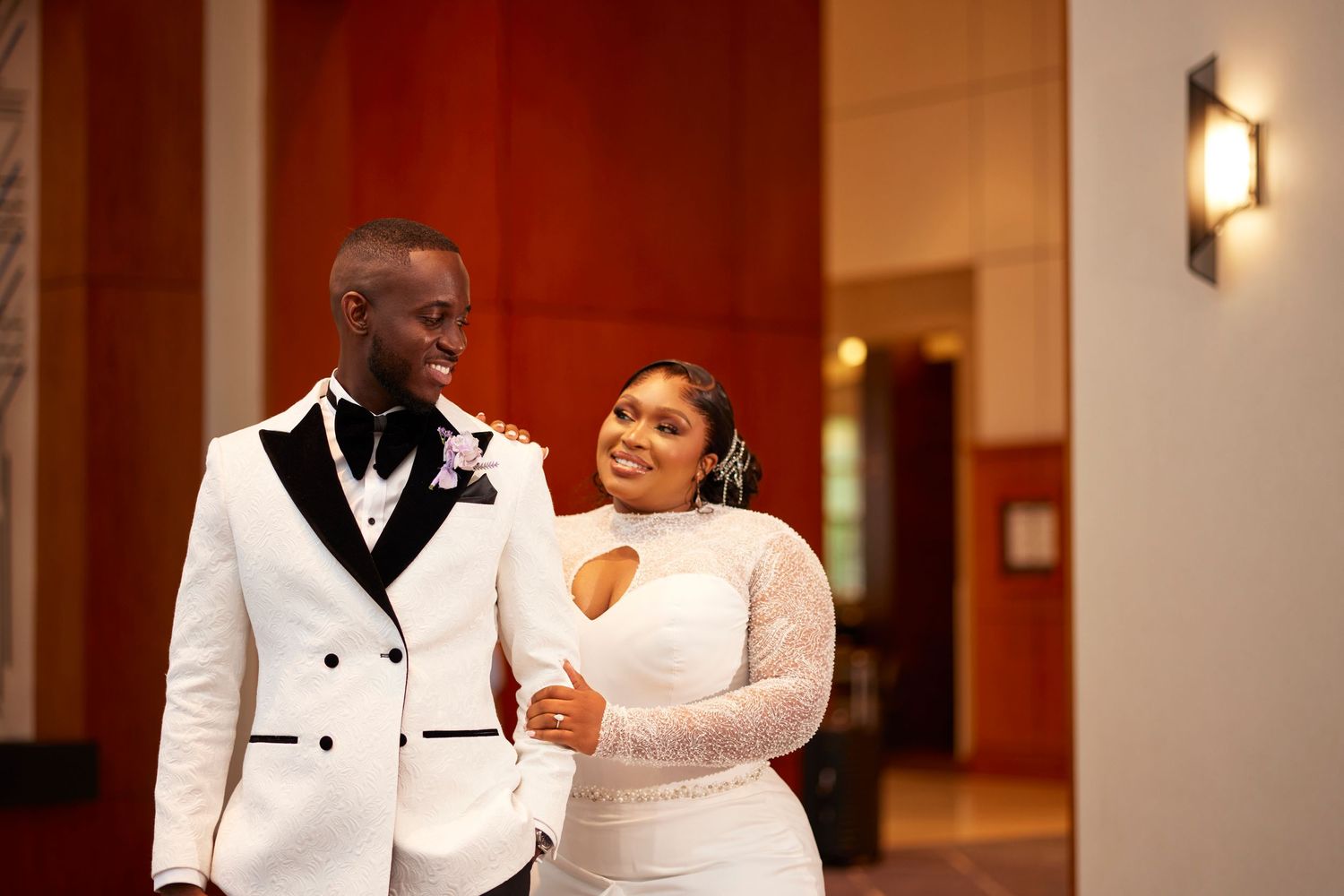 Couple in elegant white formal wear sharing a tender moment in an indoor setting.