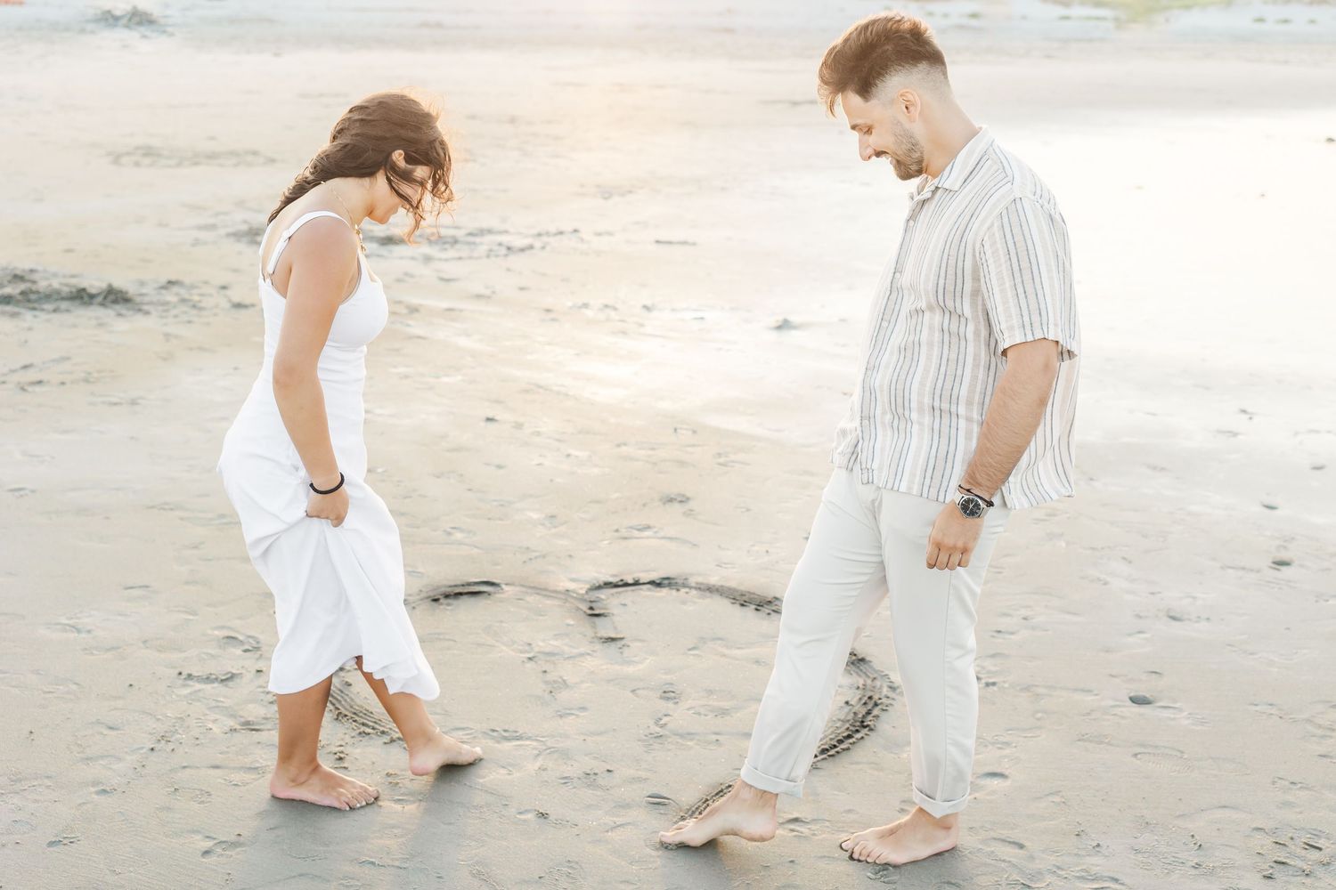 A couple walks together along a sandy beach, their footprints trailing behind them in the soft sand.