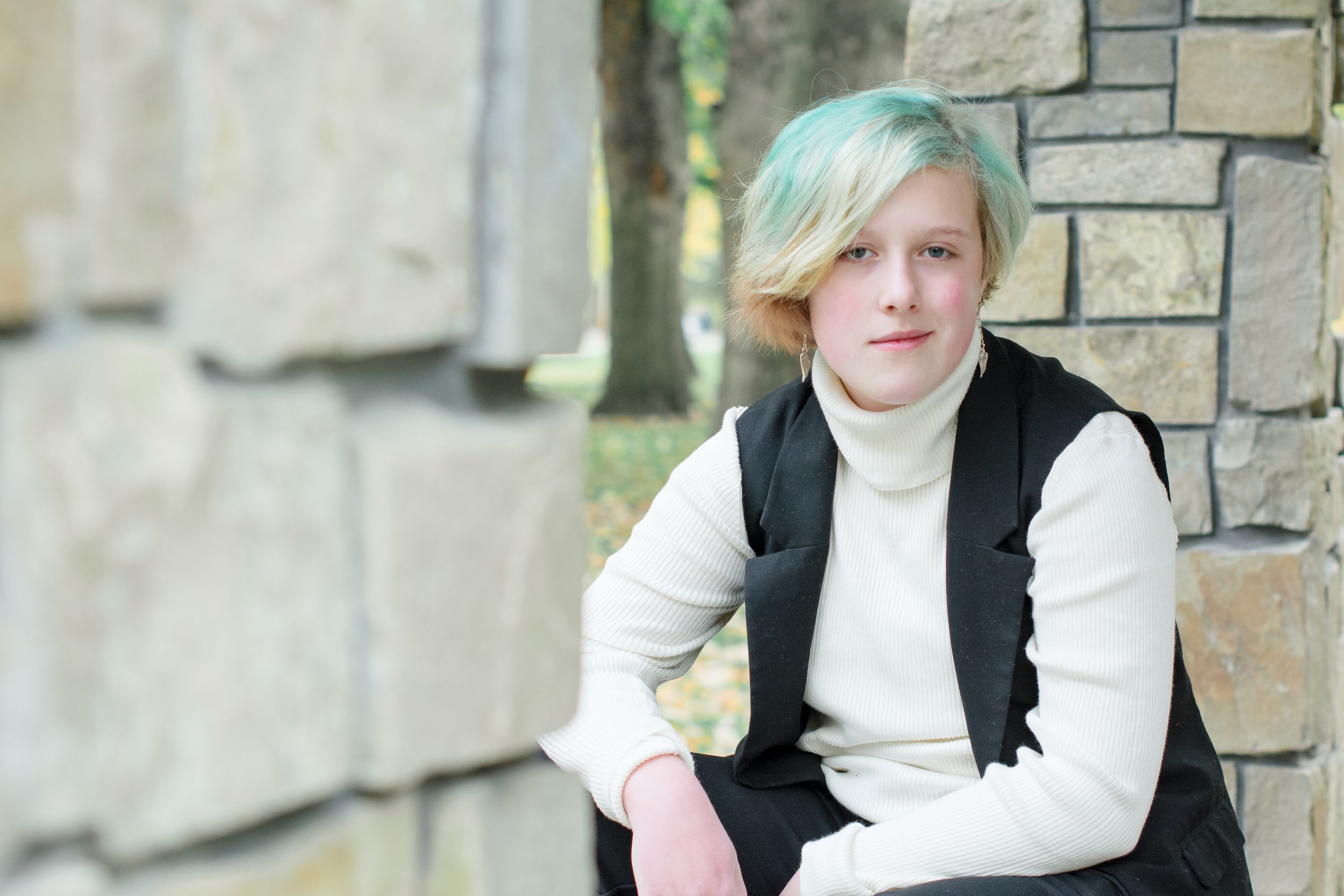 A casual portrait against a stone wall featuring light-colored clothing and natural lighting.