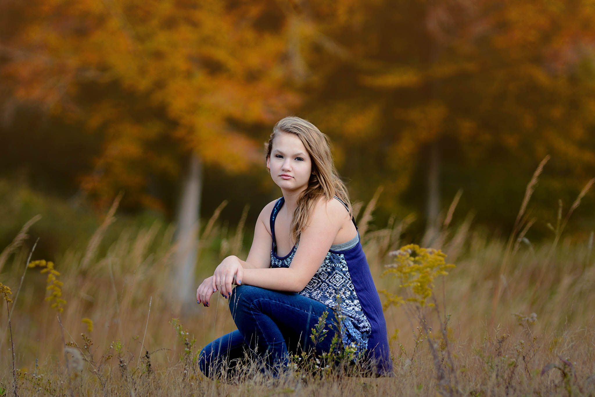 An autumn portrait in a field with colorful fall foliage in the background.