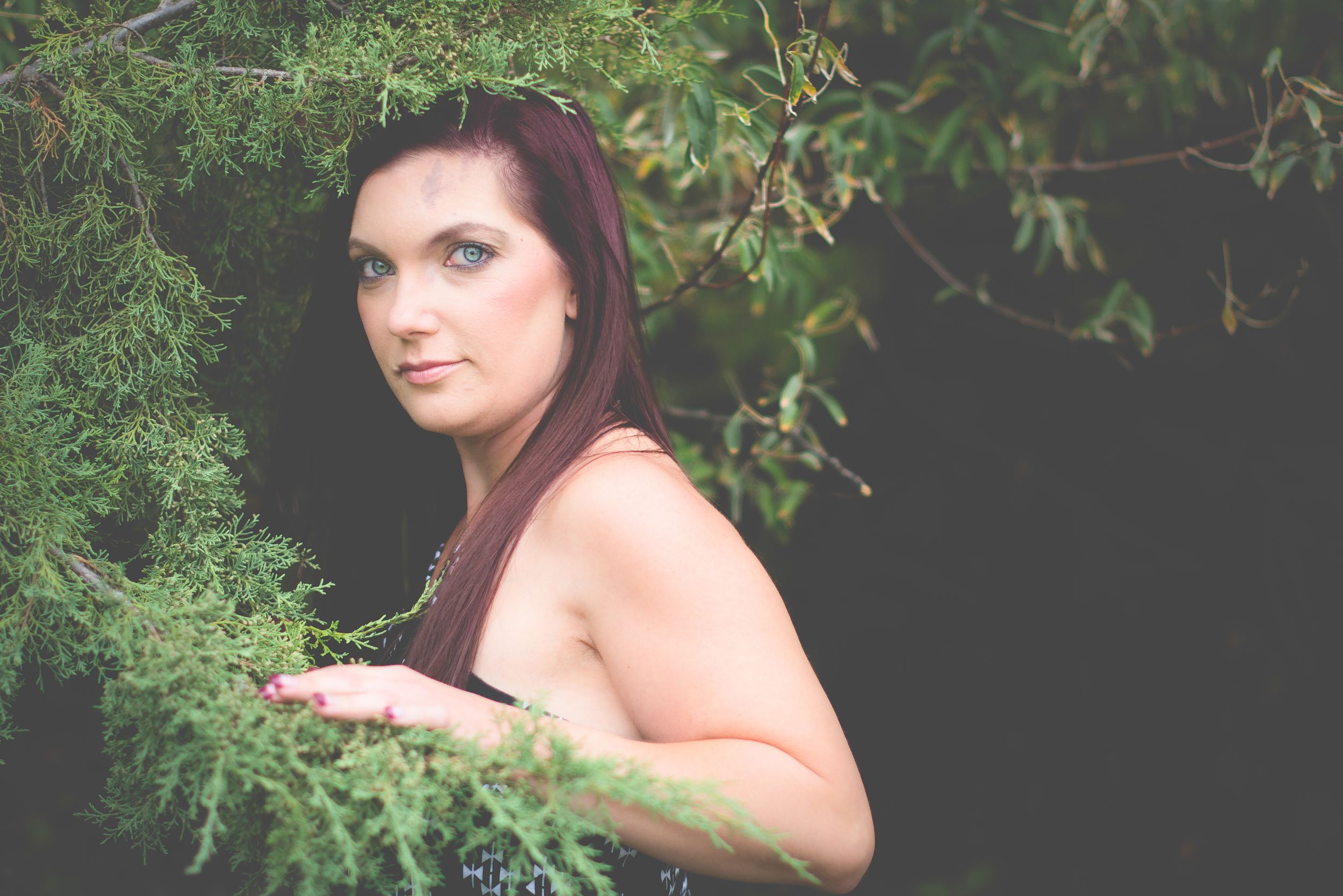 An artistic outdoor portrait with greenery and dramatic lighting in a nature setting.