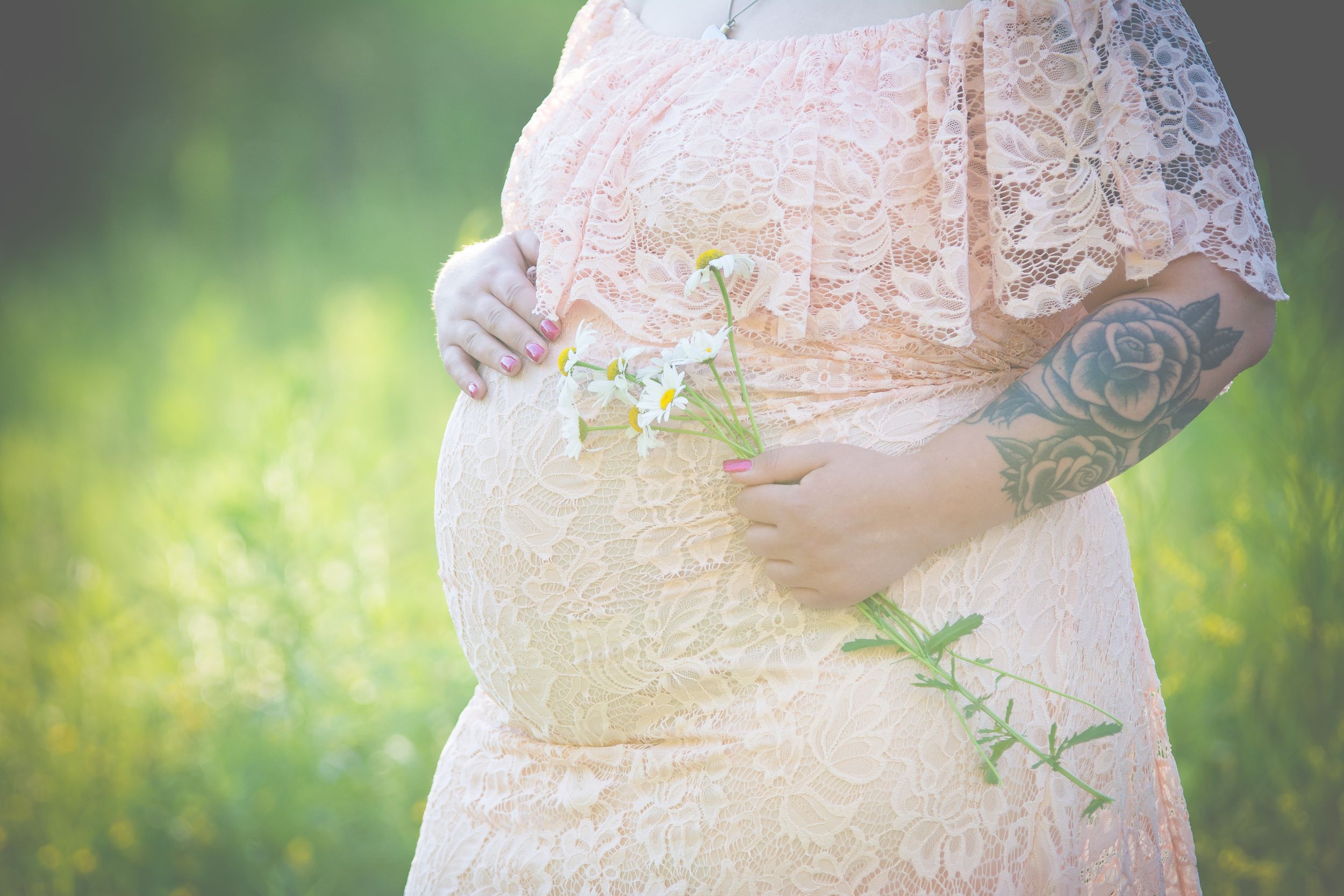 A maternity photo showing a lace dress detail with flowers against a blurred green background.