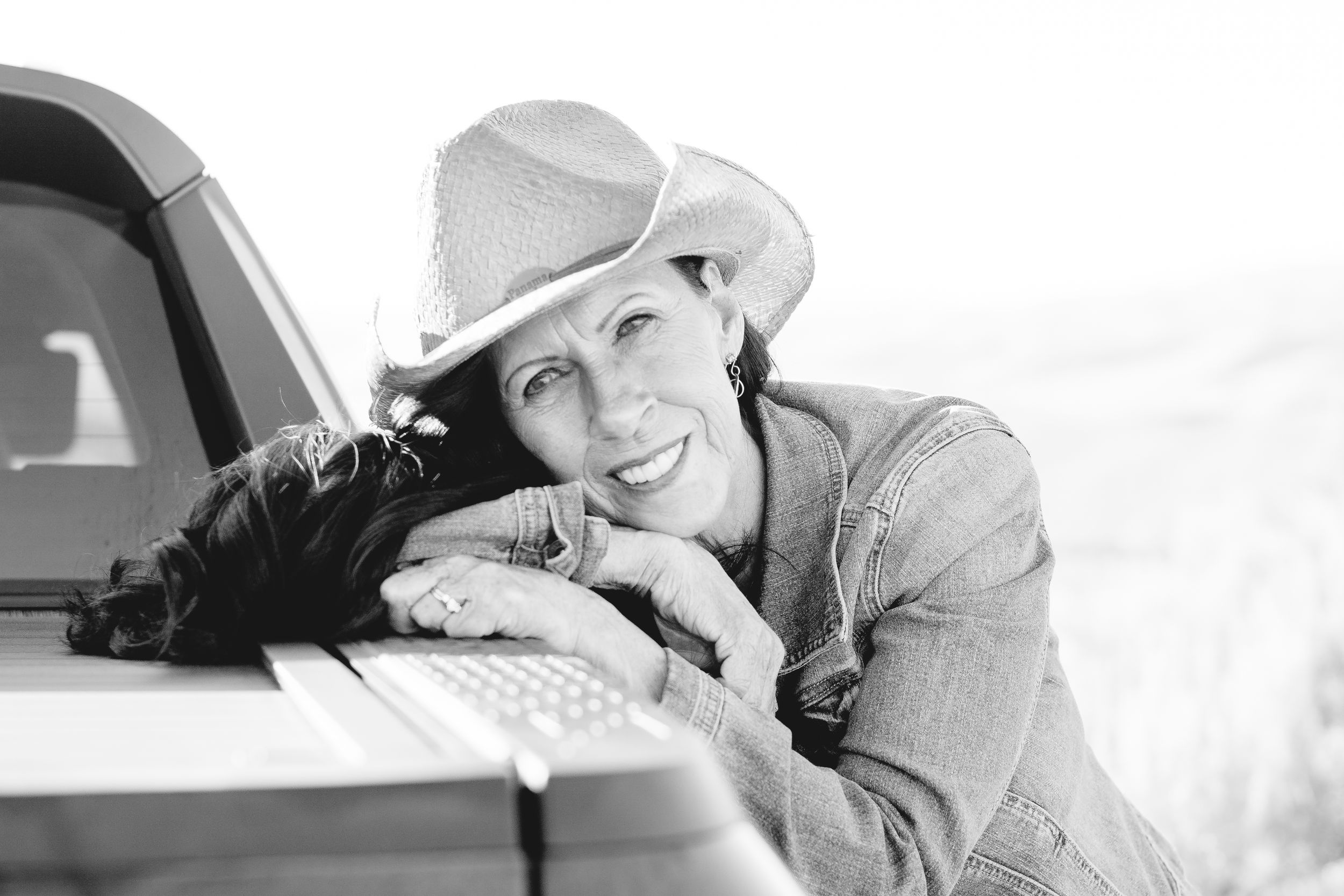 A black and white portrait leaning against a vehicle in western-style attire.