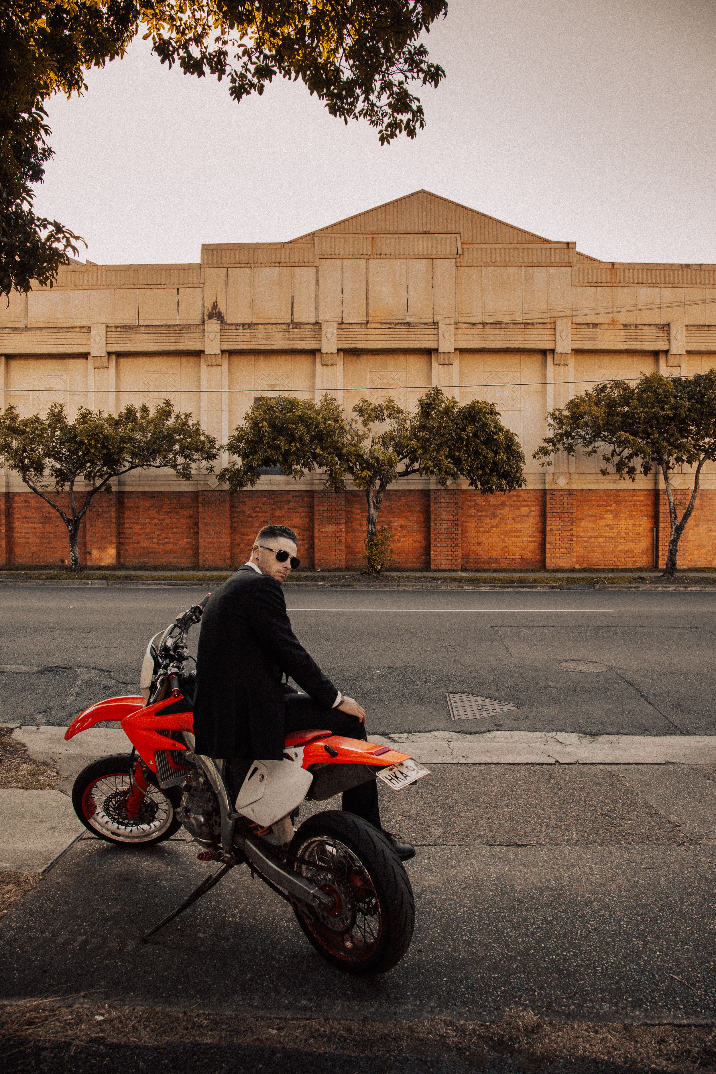 Custom motorcycle silhouetted against industrial building facade in moody evening light creates dramatic urban scene.