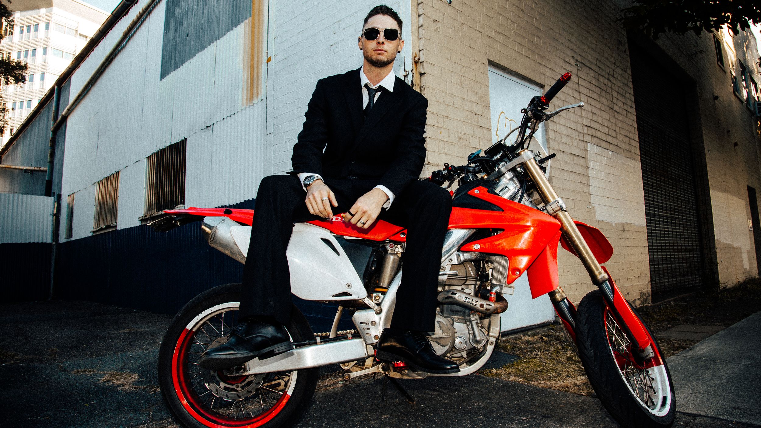 Four sequential photos showcase a bright red motorcycle parked against urban brick walls and pavement.