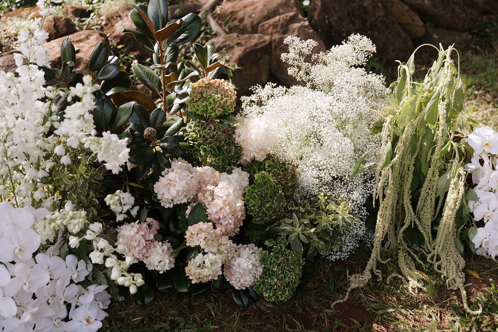 Delicate white and pink floral arrangement with greenery against natural stone backdrop.