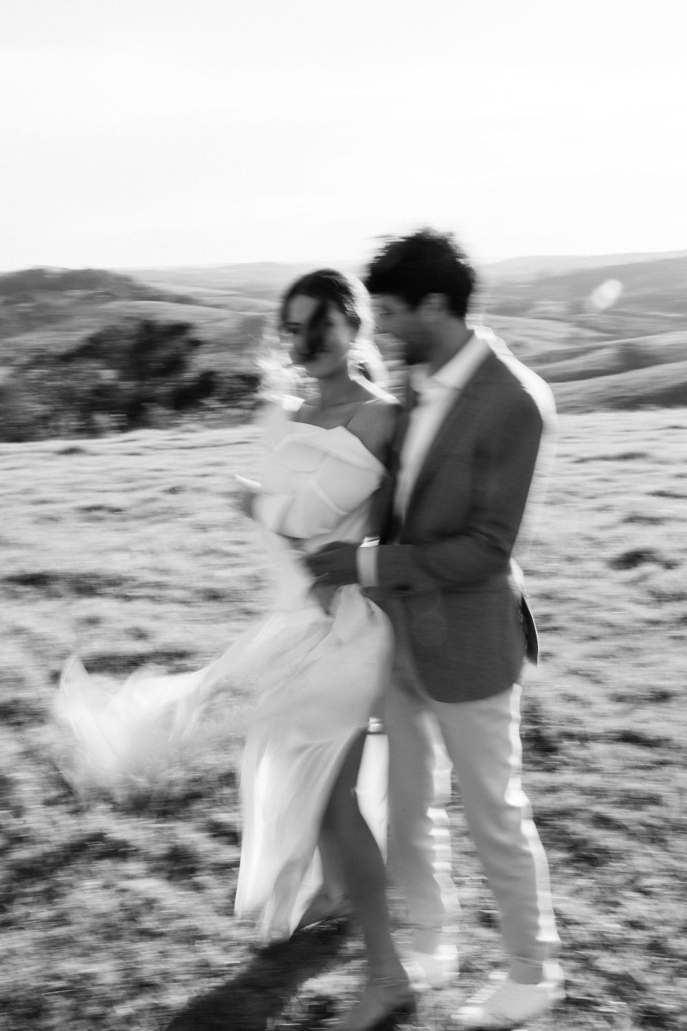 A romantic black and white photo of a couple embracing in a windswept field.