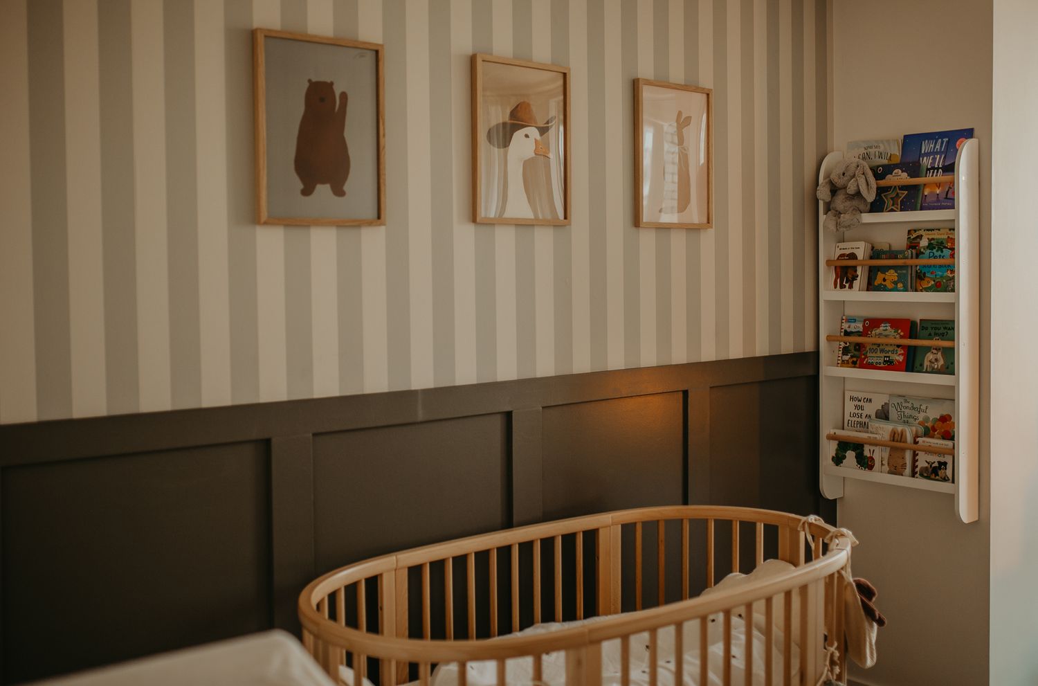 A modern nursery room with a wooden crib, neutral beige walls, and framed artwork showcases a cozy minimalist design.