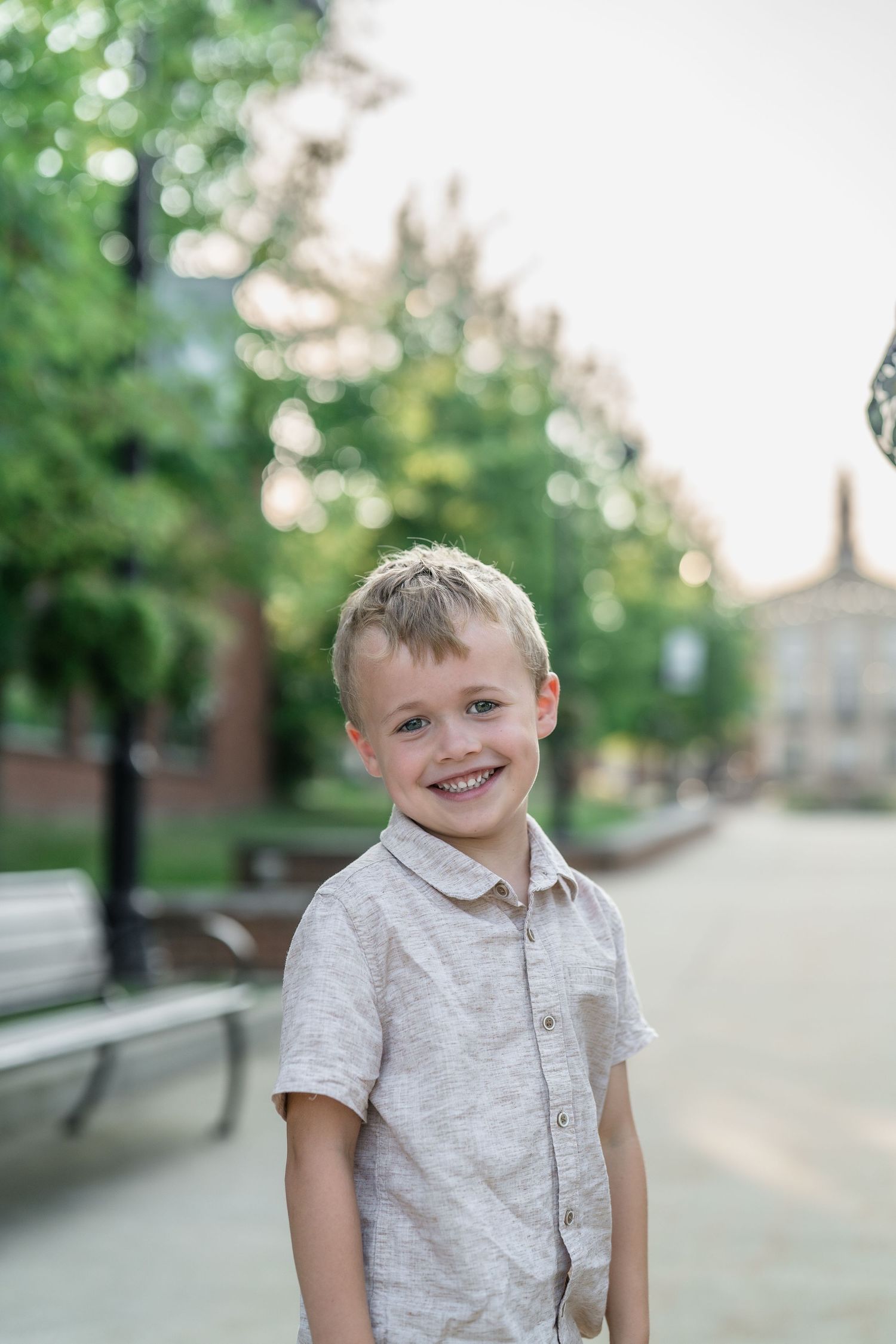 Young child smiles brightly while wearing a beige shirt outdoors in Downtown Cuyahoga Falls, Ohio for a family photo session.