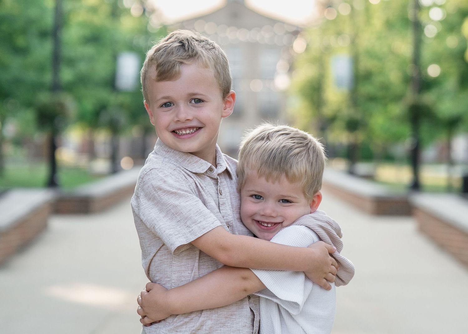 Two young boys in light colored shirts share a happy embrace while outdoors on a walkway for a Downtown Cuyahoga Falls, Ohio Family Photo