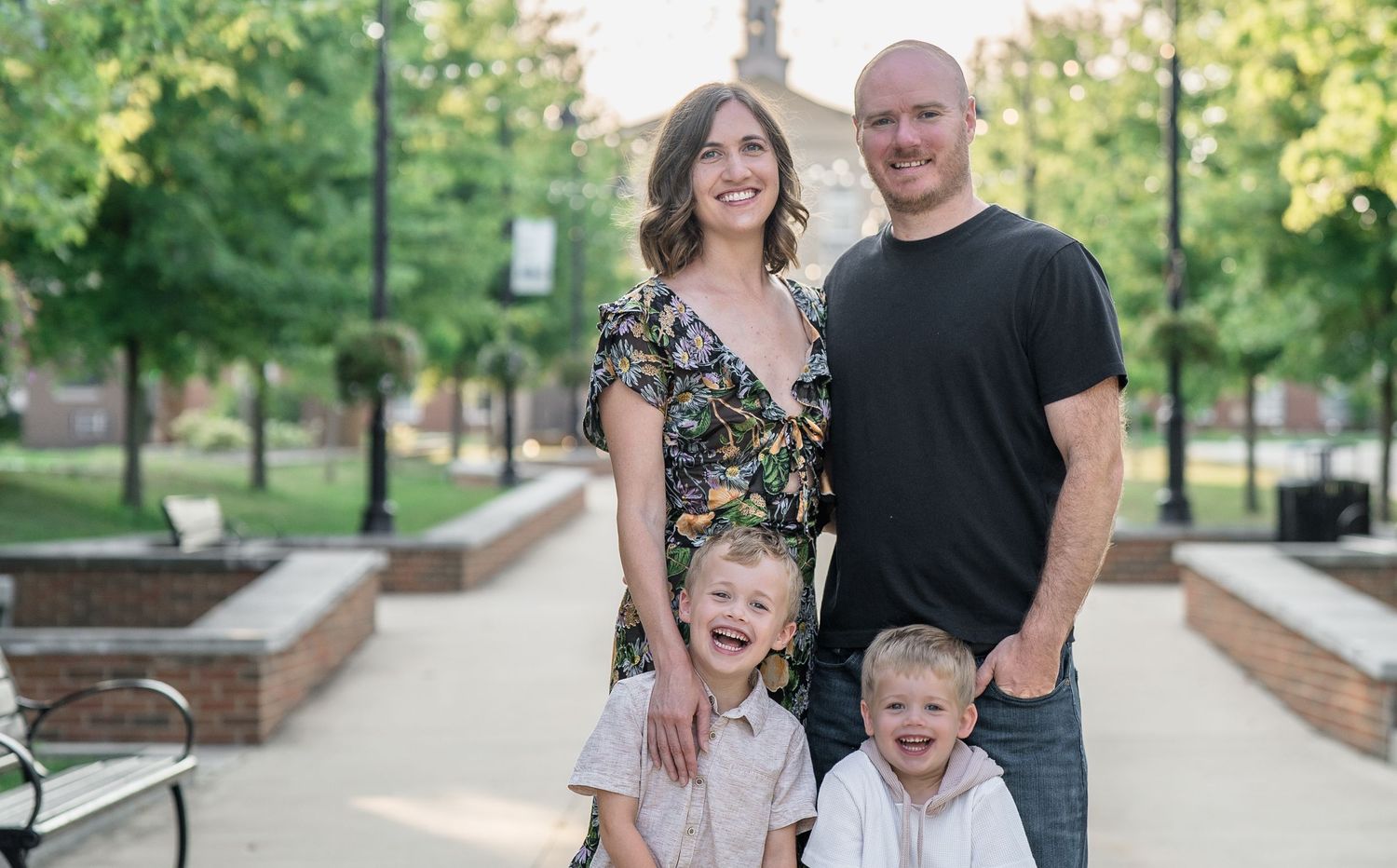 A family stands together on a paved pathway surrounded by greenery and landscaped grounds on a sunny day in Downtown Cuyahoga Falls, Ohio