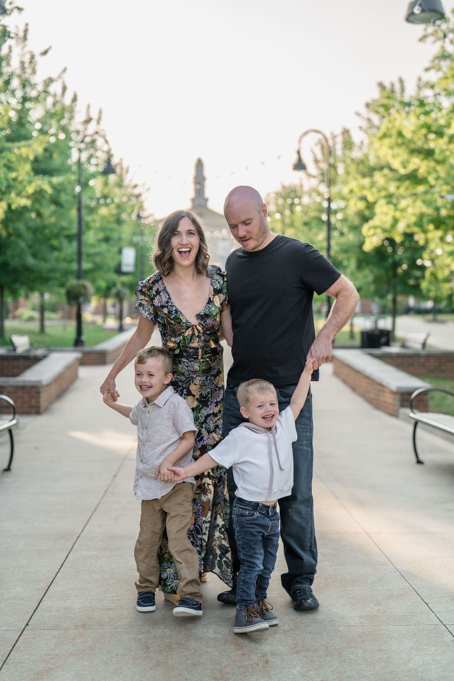 Family playing and having fun together on a concrete pathway amid greenery and sunlight at Family Session in Downtown Cuyahoga Falls, Ohio