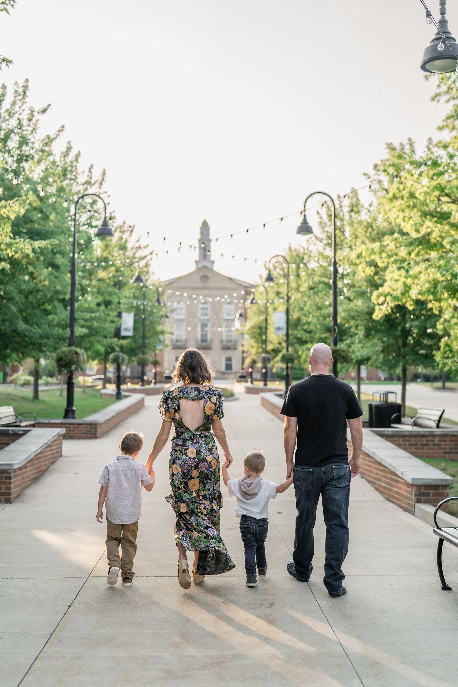 A family walks together down a path with greenery and lamp posts on a sunny day in Downtown Cuyahoga Falls with local family photographer