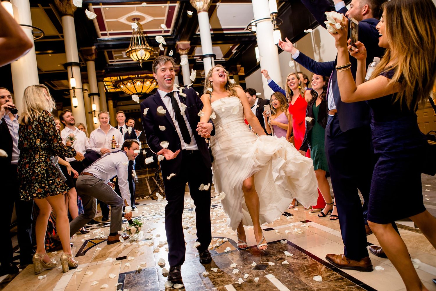 Wedding guests crowd the dance floor during a lively reception celebration with dim ambient lighting.