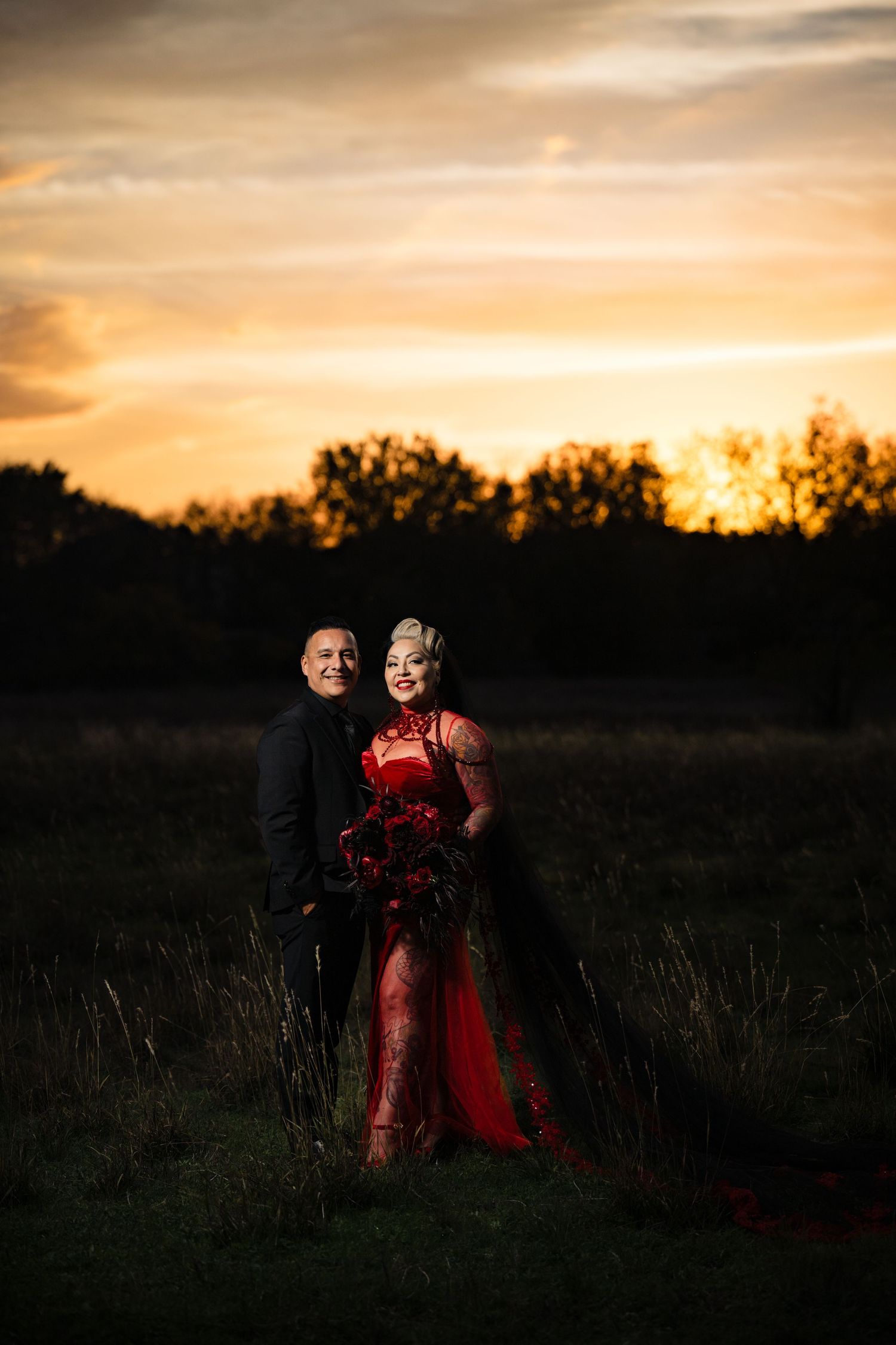 A romantic couple embraces in a field at sunset as the golden sky creates a dreamy silhouette effect.