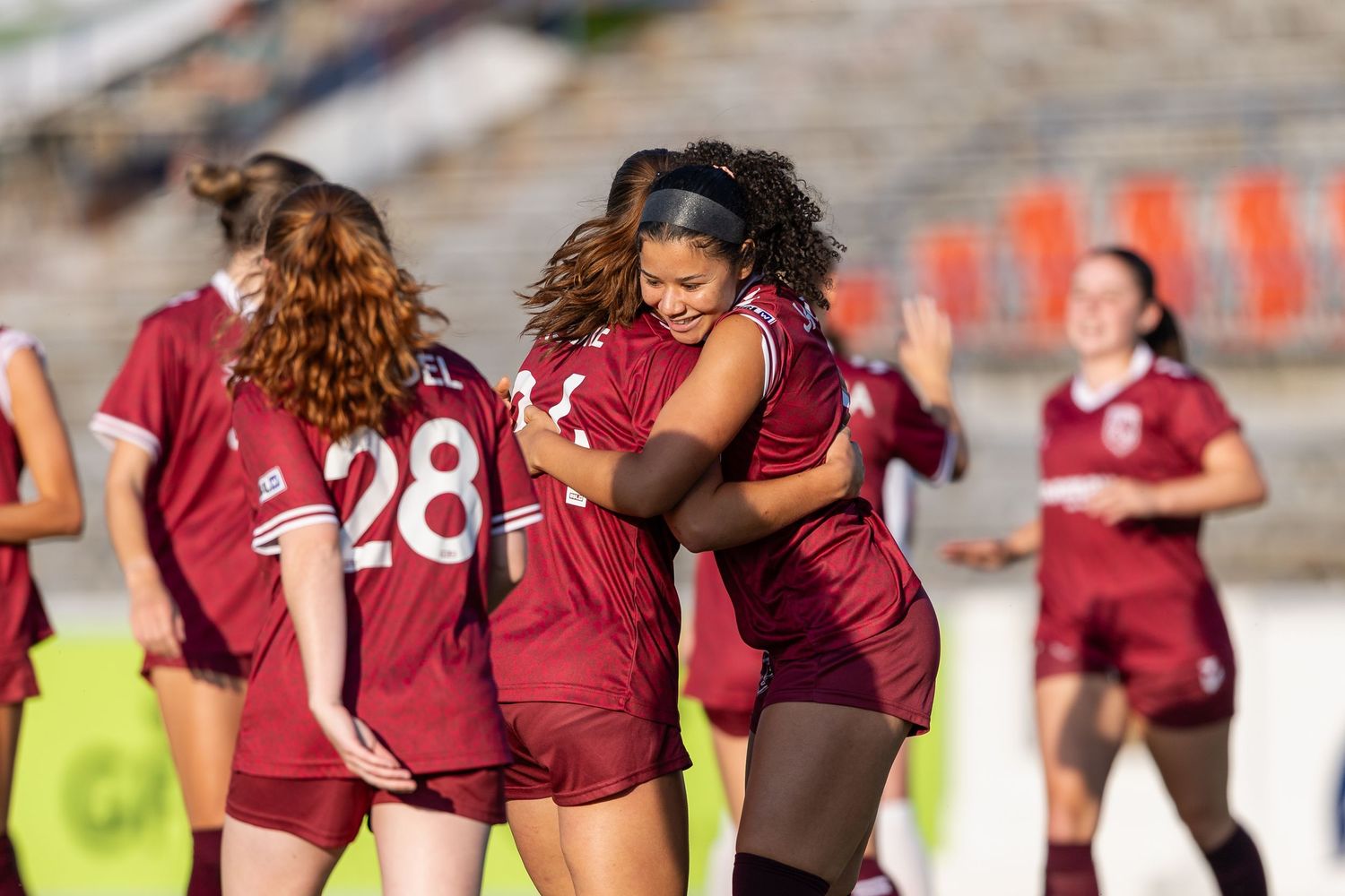 Young soccer players in white uniforms celebrate together on a sunny field.