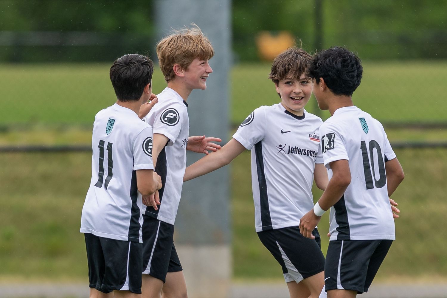 Young soccer players in white uniforms celebrate together on a sunny field.
