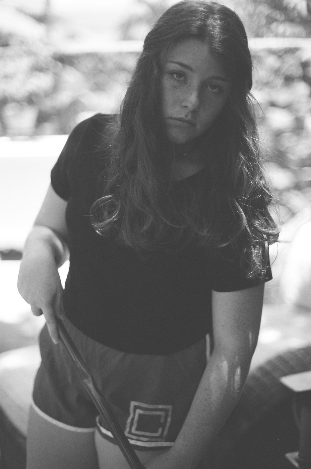 Black and white photo of a teenage girl with long hair holding a golf club outdoors.