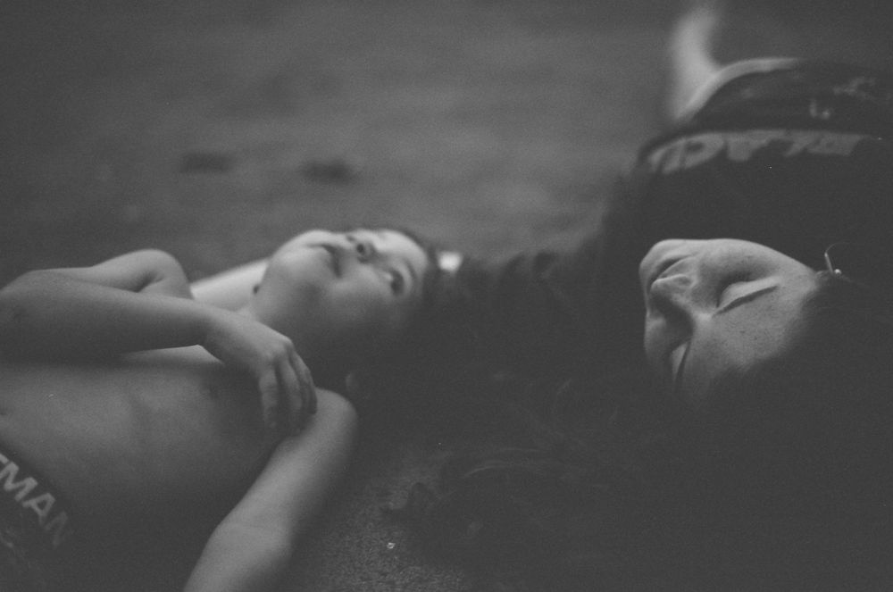 Two people lying side by side on the ground in a moody black and white outdoor photo.