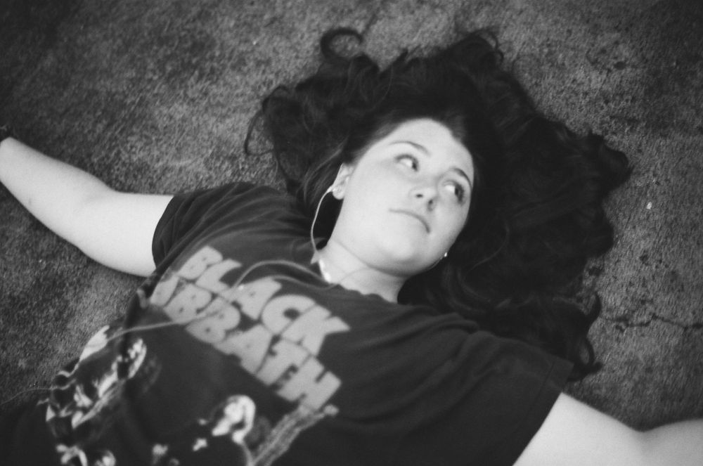 Young woman with long dark hair lying on ground wearing Black Sabbath t-shirt, black and white.