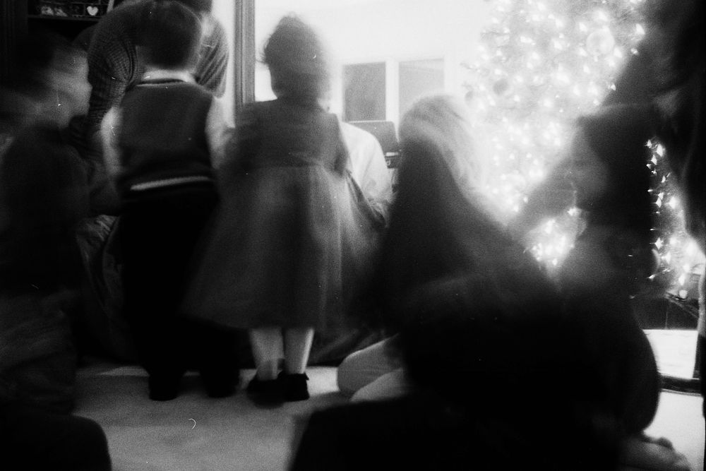 Black and white photo of children gathered around a Christmas tree near a window at a holiday gathering.