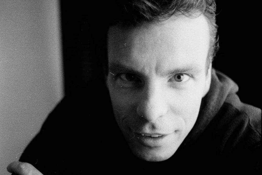 Close-up black and white portrait of a young man in a dark hoodie looking at the camera.