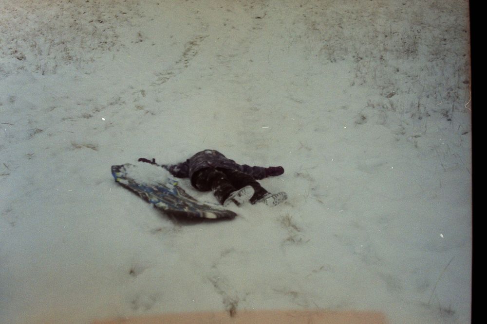 A dog lying in the snow next to a bird, captured in a vintage outdoor photograph.
