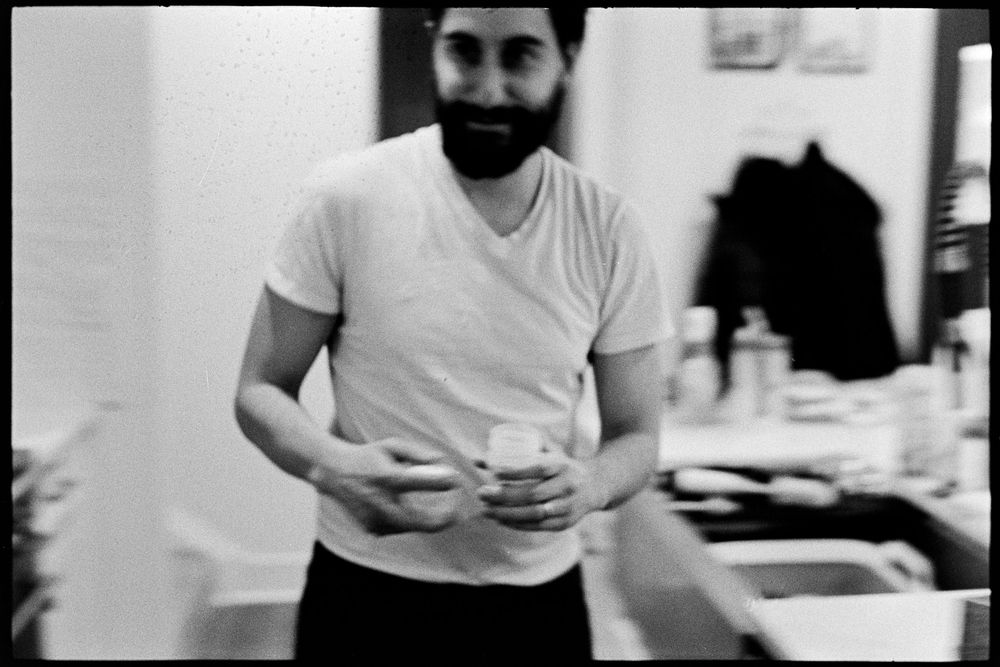 Bearded man in white v-neck t-shirt holds small object in black and white photo.