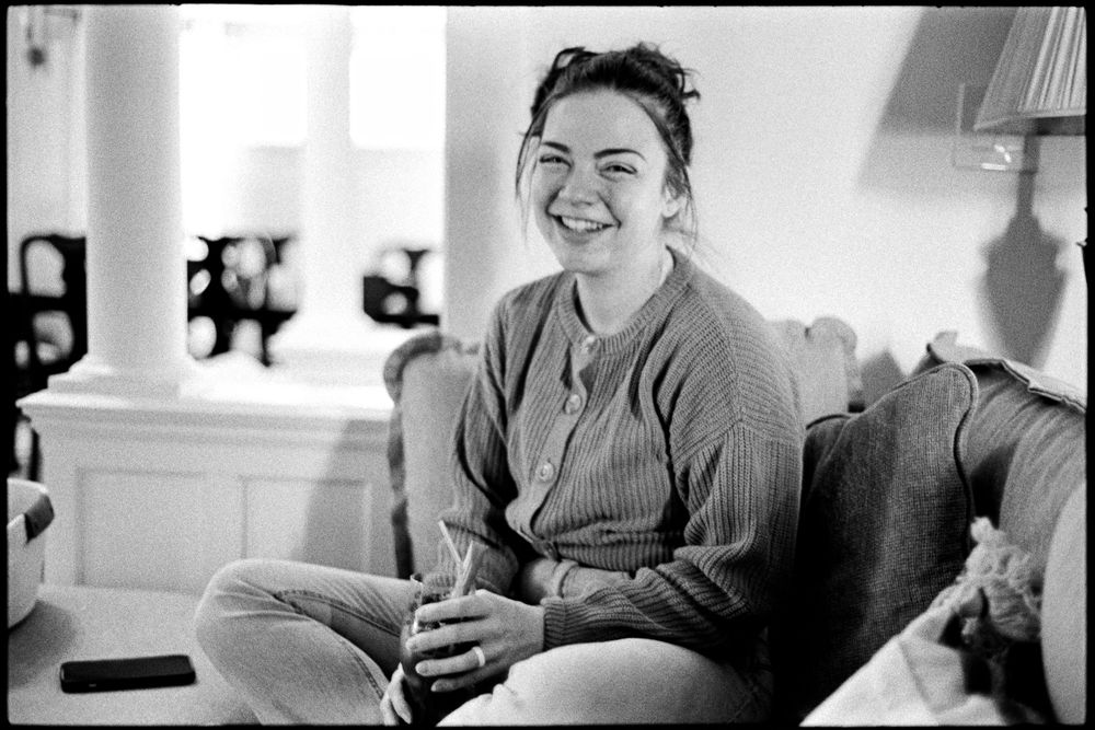 Black and white portrait of smiling young woman sitting cross-legged on sofa indoors.