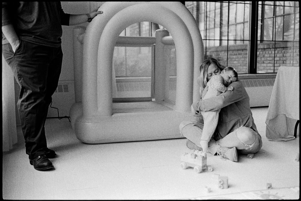 Parent hugging child near an inflatable arch in a bright white room, black and white photo.