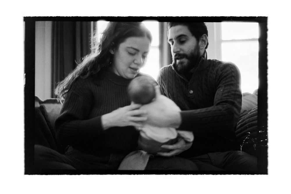 Black and white photo of new parents tenderly holding their newborn baby together on a couch.