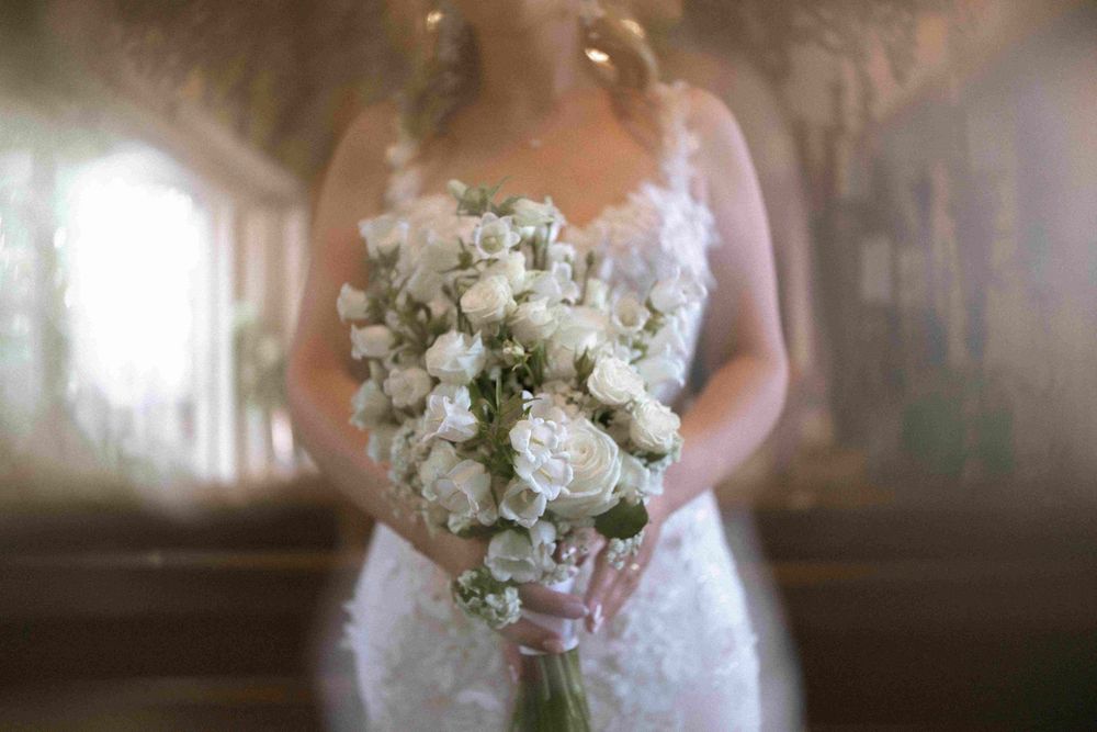 An elegant white wedding bouquet of mixed flowers held against a dreamy background.