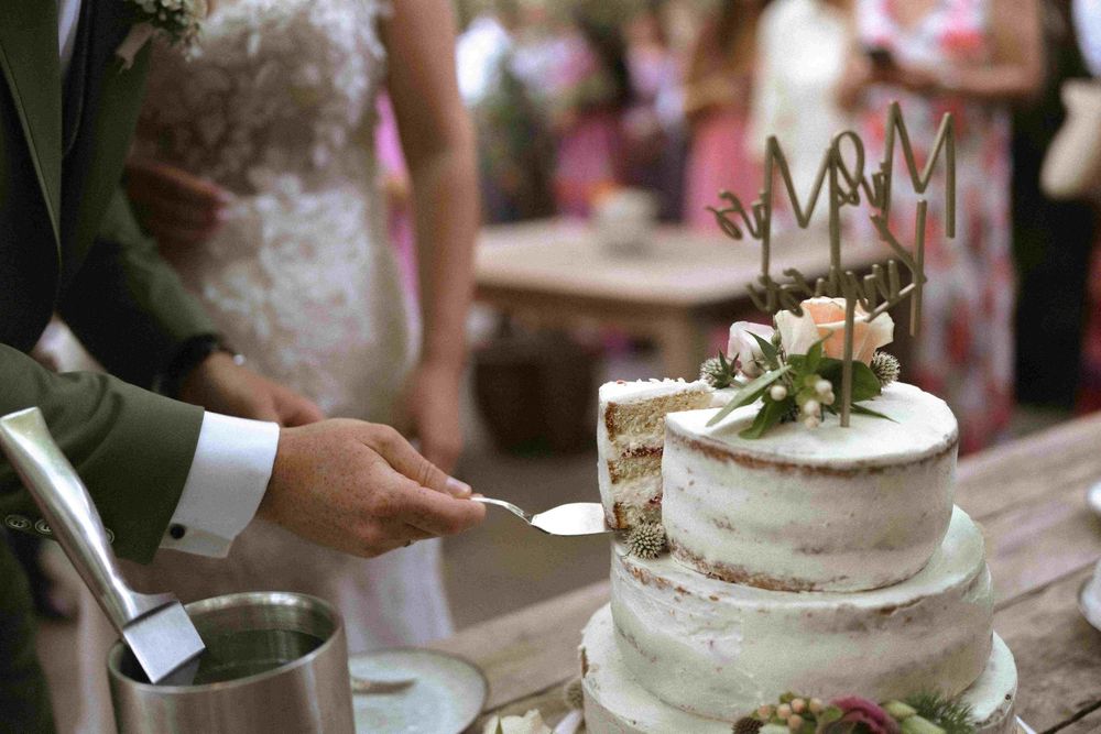 Wedding cake cutting scene with white tiered cake decorated with flowers and crown topper.