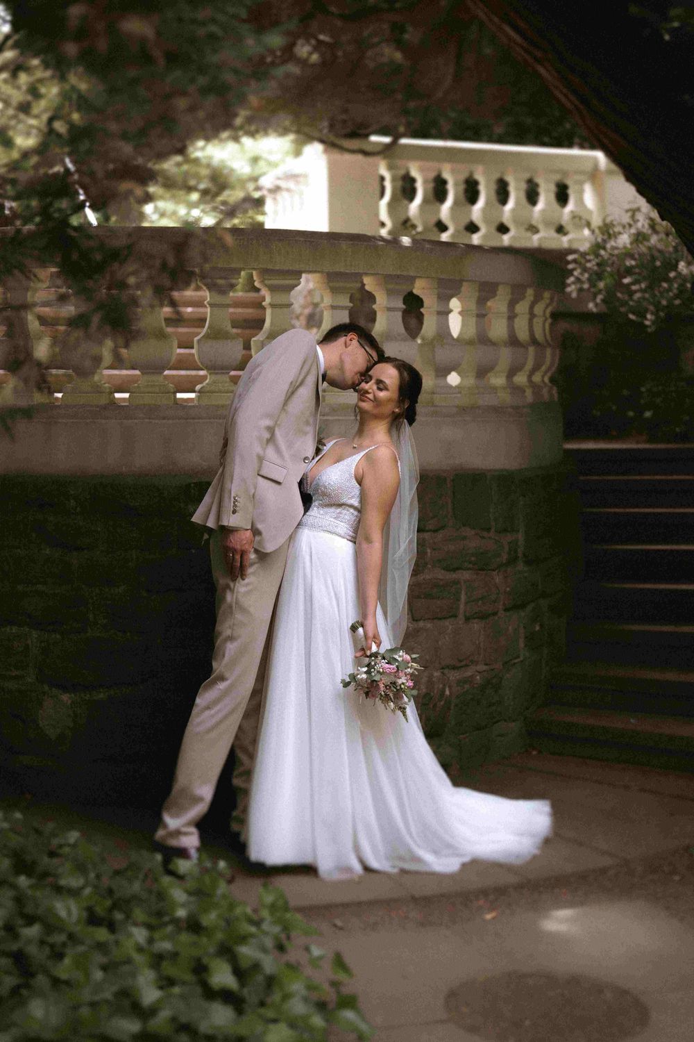 Romantic wedding portrait on stone steps with ornate balustrade backdrop.