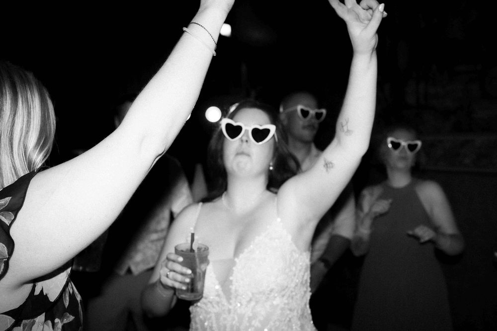 Wedding reception guests dancing and celebrating while wearing sunglasses.