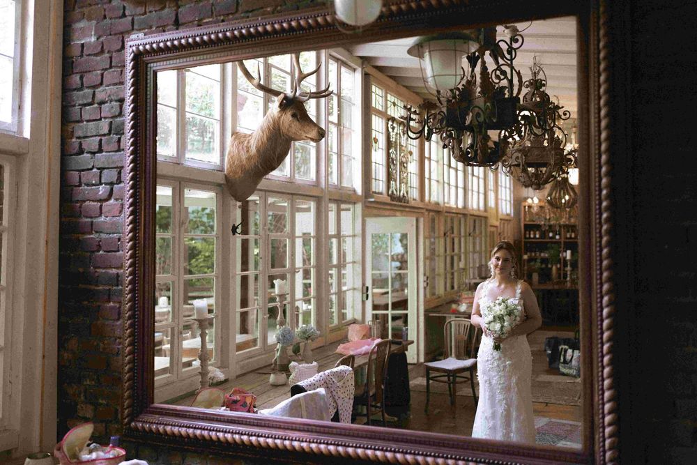 Reflection in an ornate mirror shows a bridal preparation room with deer head decor.