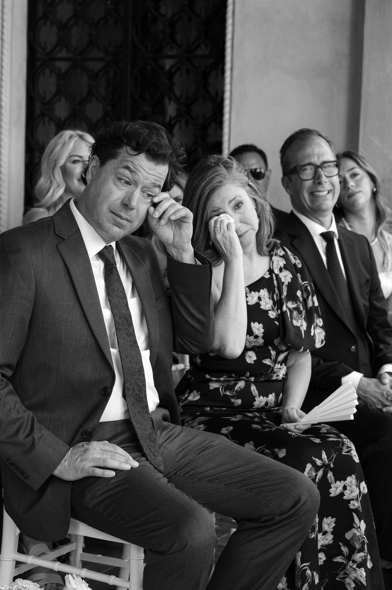 Wedding guests laughing and enjoying themselves while seated in formal attire at an event.