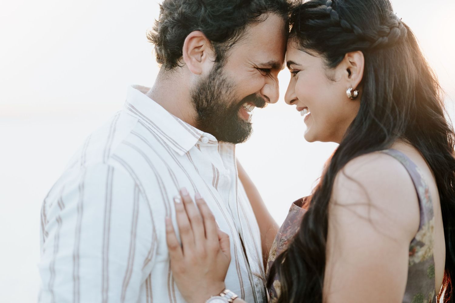 A couple shares an intimate moment while smiling and embracing each other outdoors.
