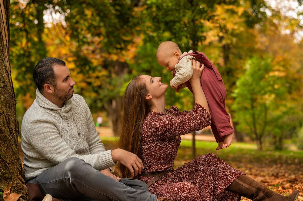A family enjoys playful moments together on fallen autumn leaves in a park setting.