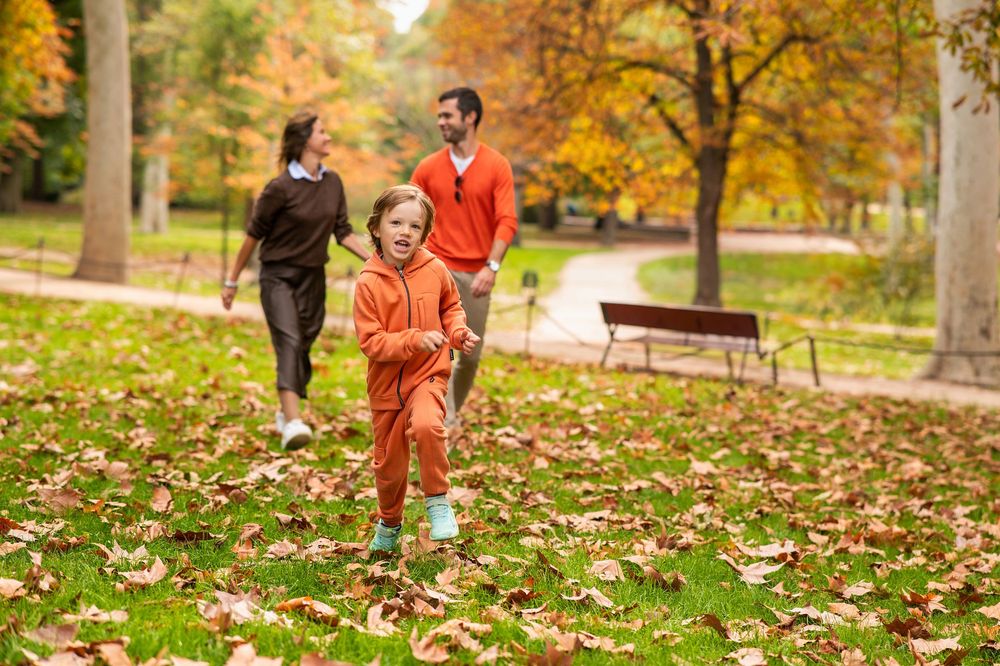 People walk along a tree-lined path with vibrant orange fall foliage in a park setting.