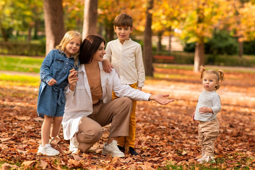 A family spends quality time playing in fallen autumn leaves on a sunny afternoon in the park.