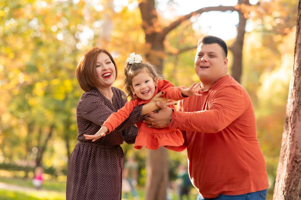 A happy family plays together outdoors during autumn with golden leaves and sunlight in the background.