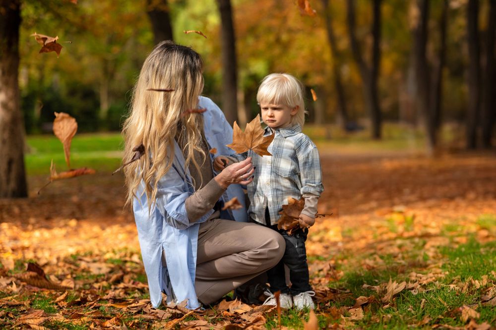 A parent and child share a tender moment while playing with autumn leaves in a park on a fall day.